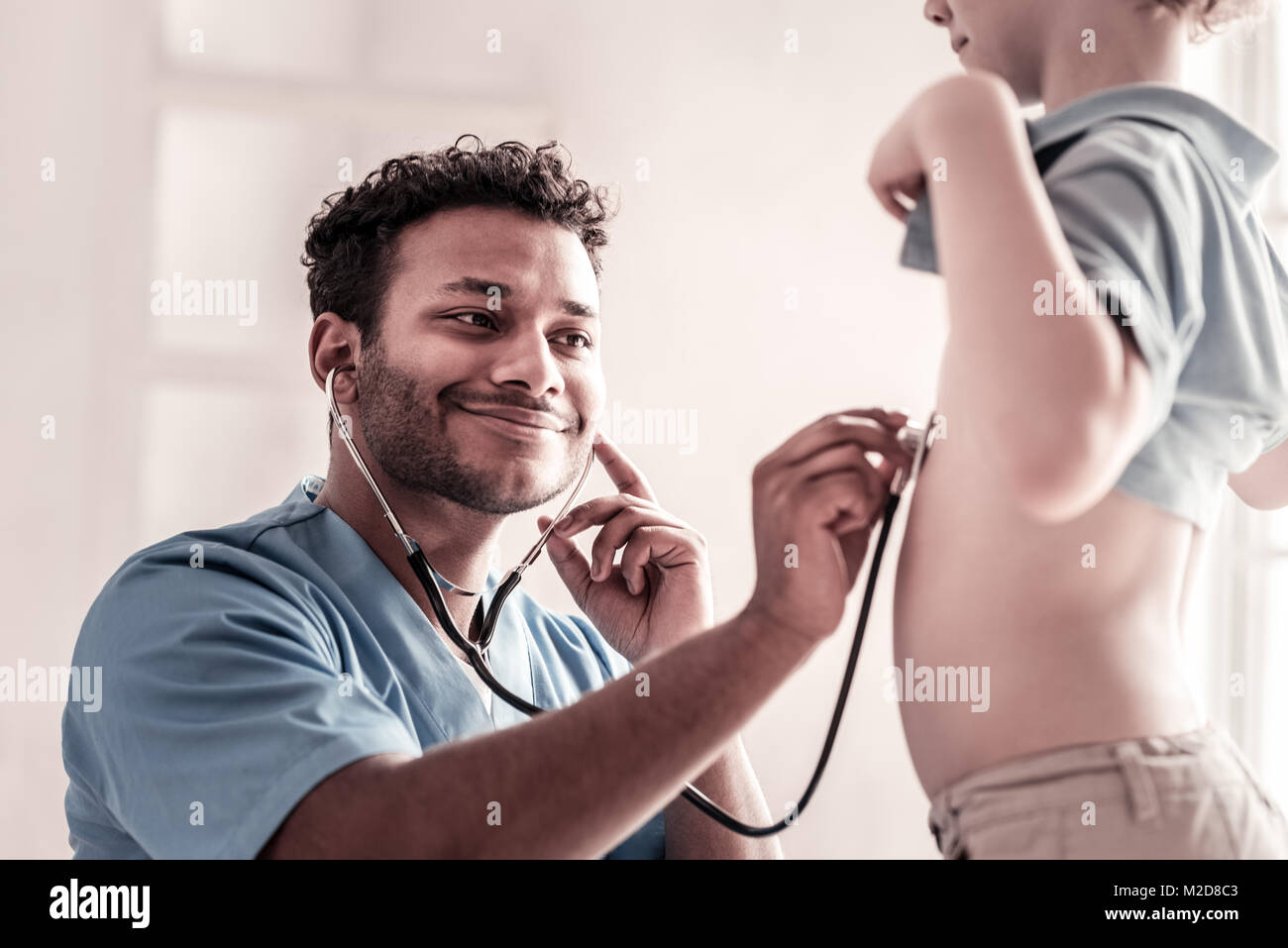 Freundlich aussehenden medizinischer Arbeiter hören zu Herzen von Kind Stockfoto