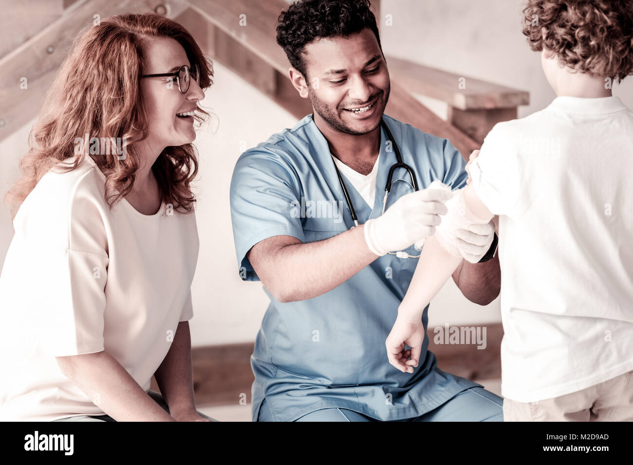 Dankbar Mutter lächelnd während Arzt bandagieren Arm ihres Sohnes Stockfoto