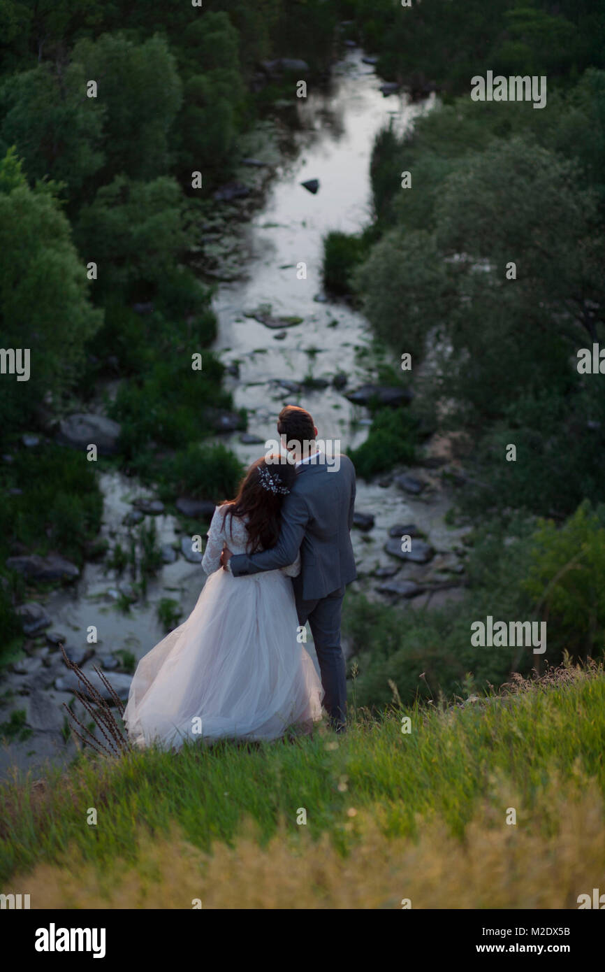 Kaukasische Braut und Bräutigam stehen auf Hügel bewundern Fluss Stockfoto