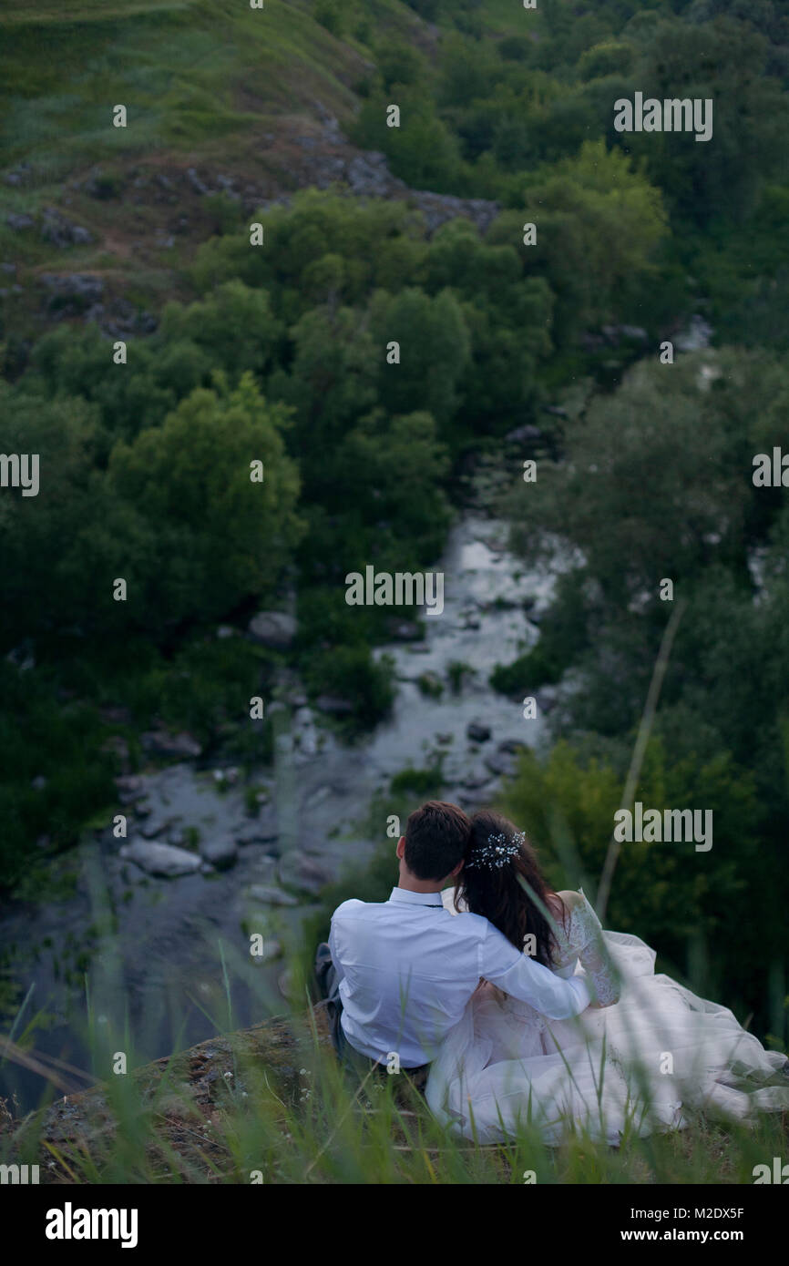 Kaukasische Braut und Bräutigam sitzen auf einem Hügel bewundern Fluss Stockfoto