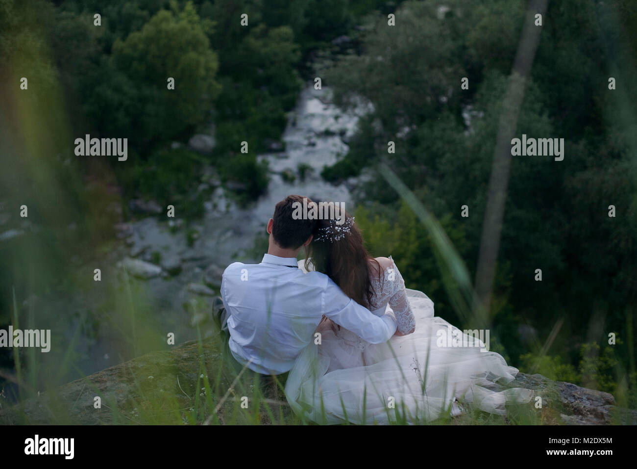 Kaukasische Braut und Bräutigam sitzen auf einem Hügel bewundern Fluss Stockfoto