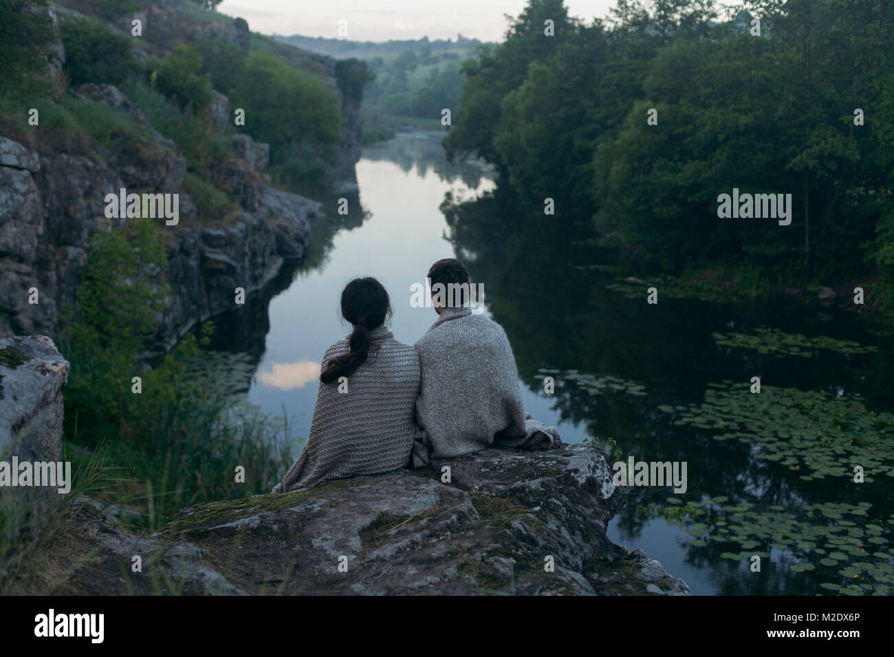 Kaukasische Paar in der Decke sitzt auf Felsen bewundern Fluss gewickelt Stockfoto