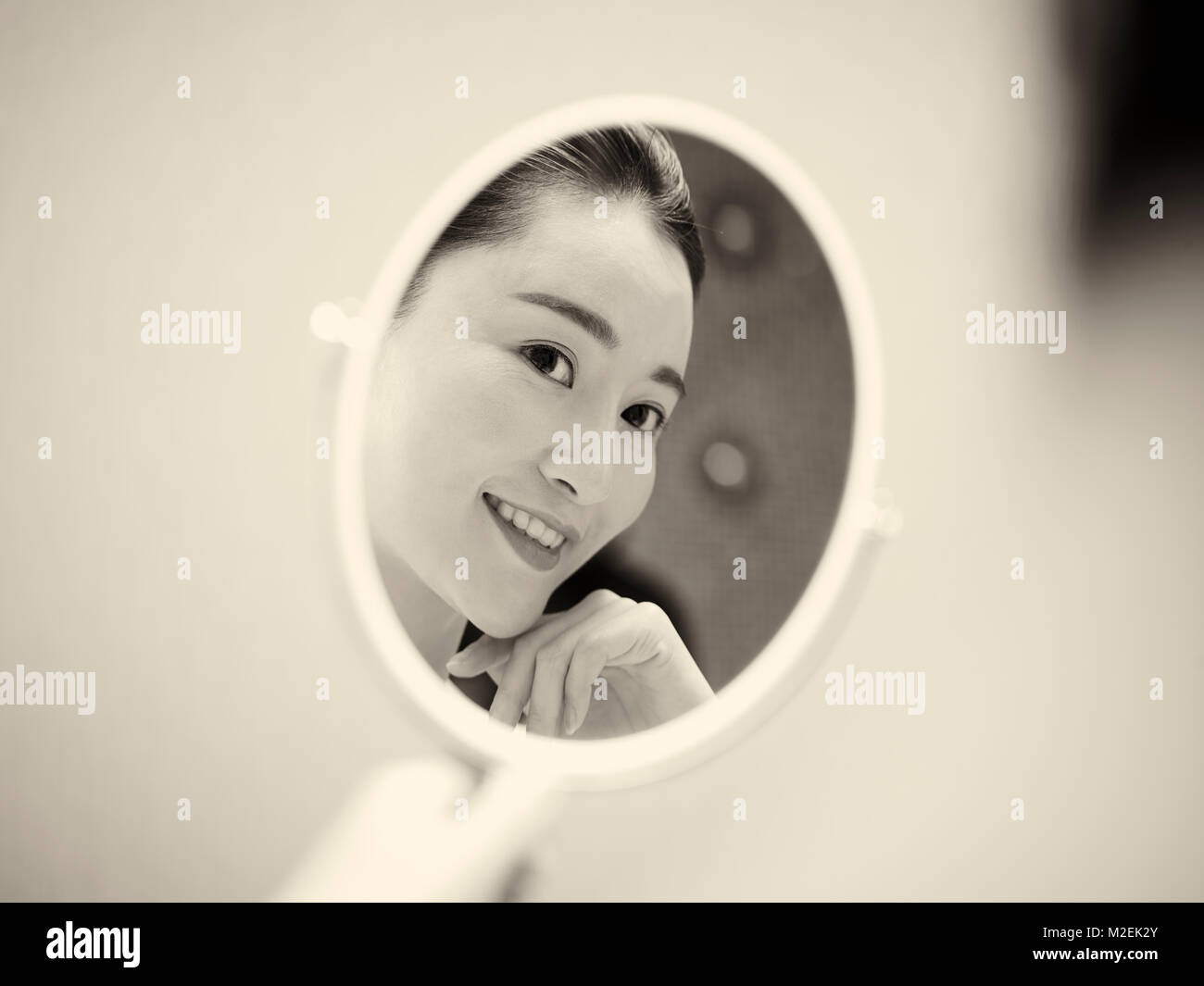 Schöne junge asiatische Frau an sich selbst im Spiegel zu betrachten, glücklich und lächelnd, Schwarz und Weiß, retro style. Stockfoto