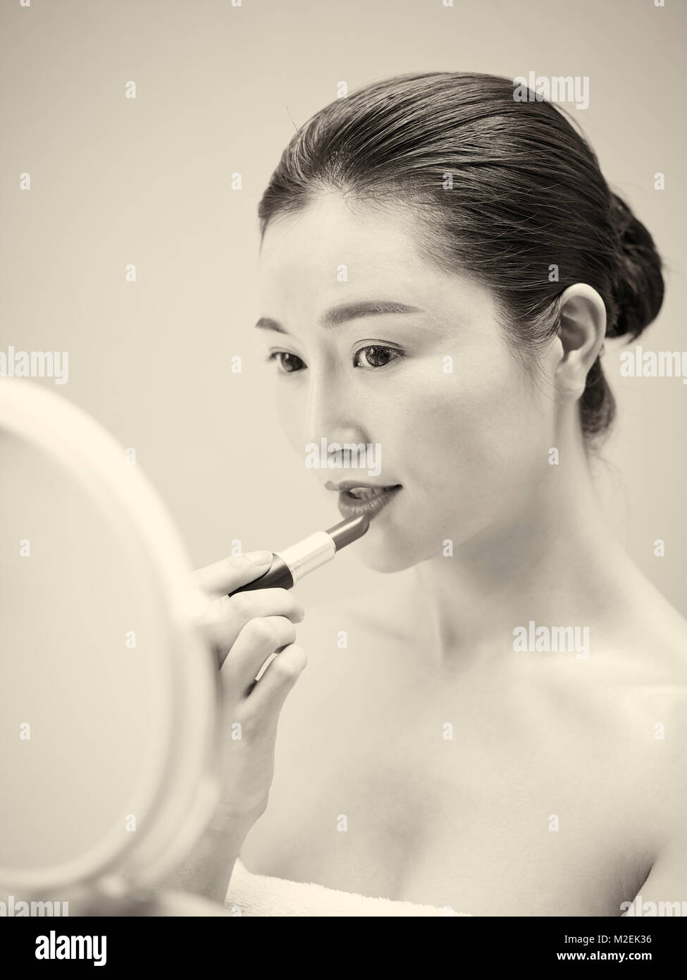 Schöne junge asiatische Frau im Spiegel zu betrachten, während die Lippen Lippenstift, Schwarz und Weiß, retro style. Stockfoto