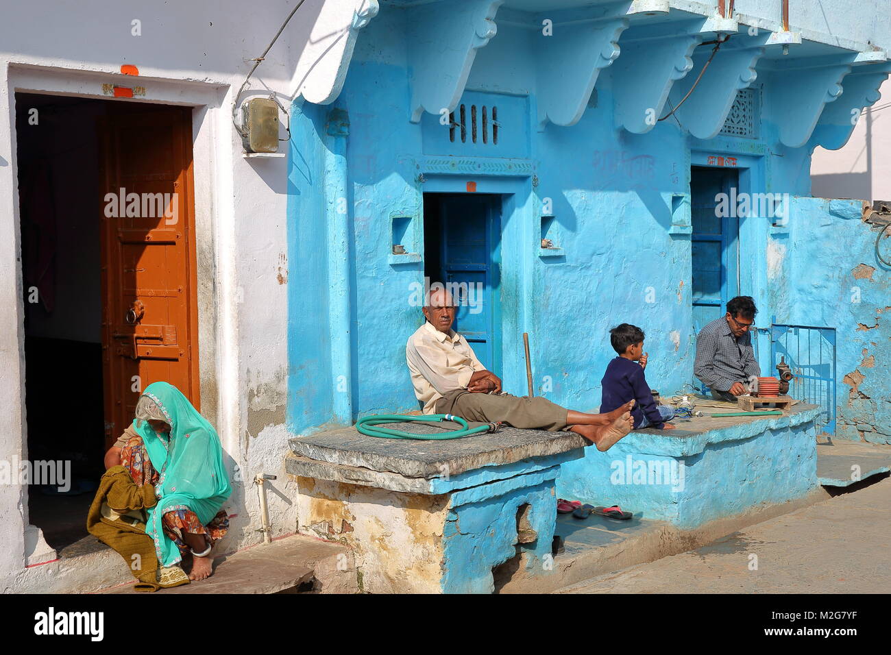 CHITTORGARH, Rajasthan, Indien - Dezember 13, 2017: Bunte Straßenszene mit Menschen die Sonne geniessen, die außerhalb ihrer traditionellen Haus Stockfoto