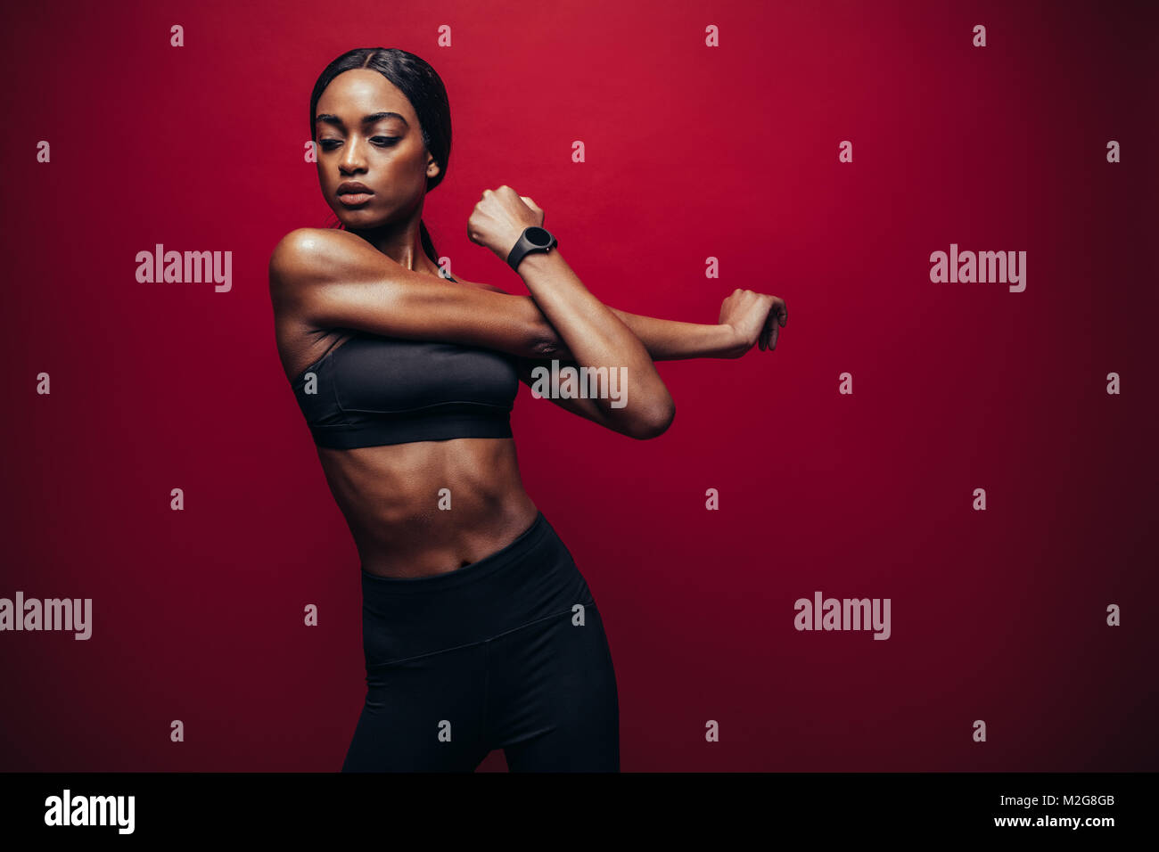 Gesunde schwarze Frau tragen fitness Outfit auf rotem Hintergrund und strecken ihre Arme. Afrikanische Frauen tun stretching Übung. Stockfoto