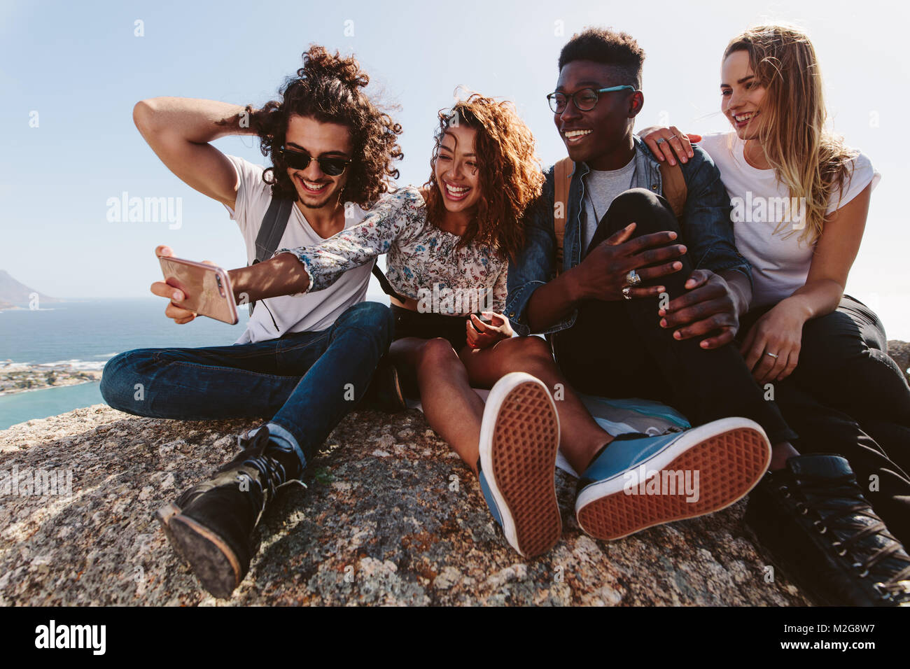 Eine Gruppe von Freunden zusammen sitzen am Berg und unter Selbstportrait mit Handy. Junge Männer und Frauen, die selfie auf Urlaub. Stockfoto