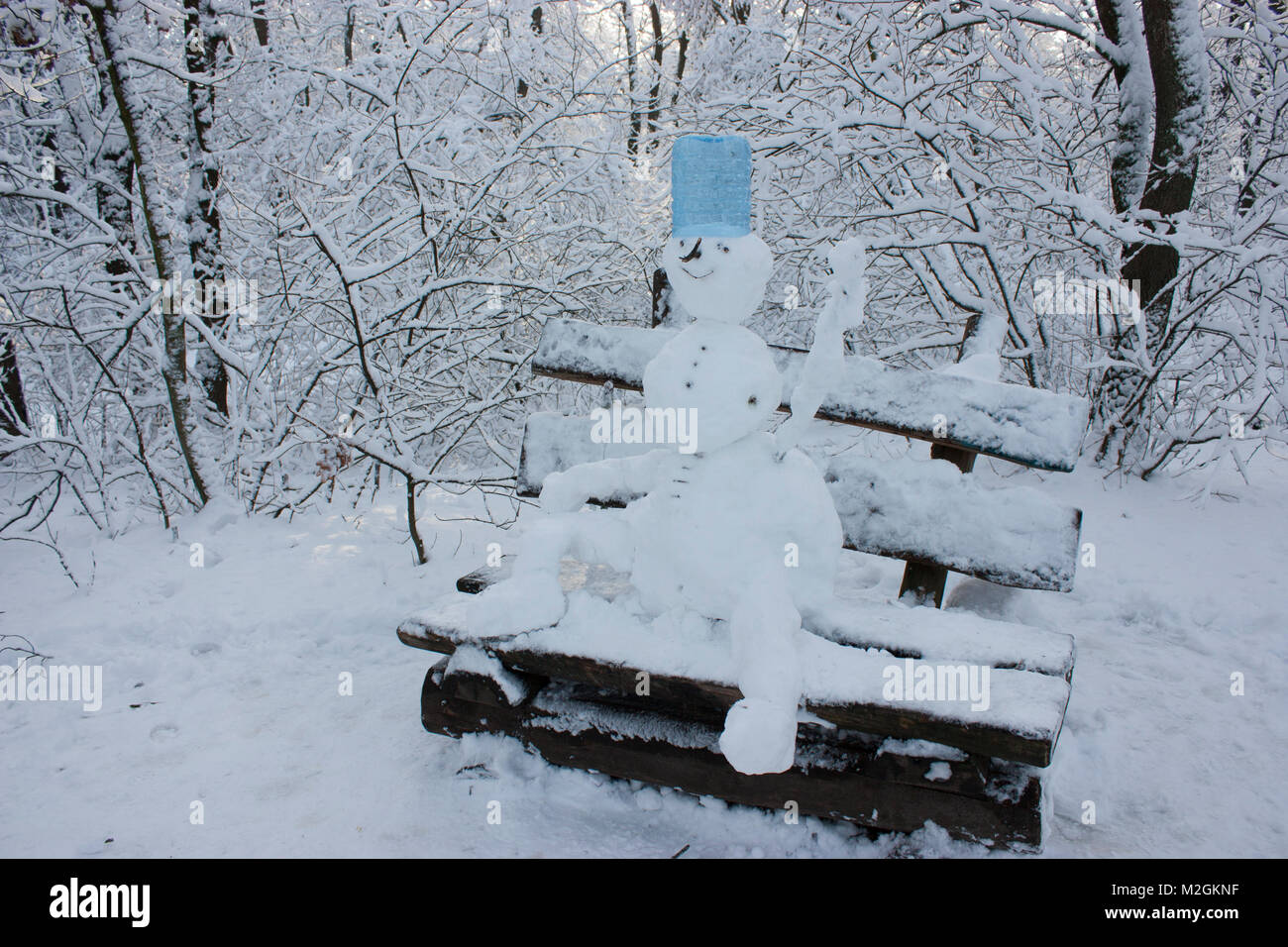 Schneemann sitzt auf einer Bank im Wald im Winter, viel Schnee, Bäume im Schnee Stockfoto