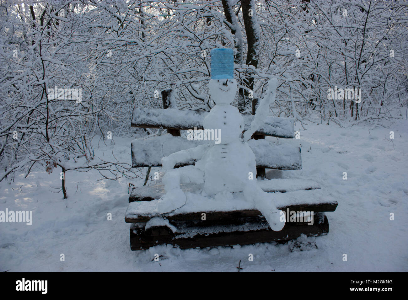 Schneemann sitzt auf einer Bank im Wald im Winter, viel Schnee, Bäume im Schnee Stockfoto