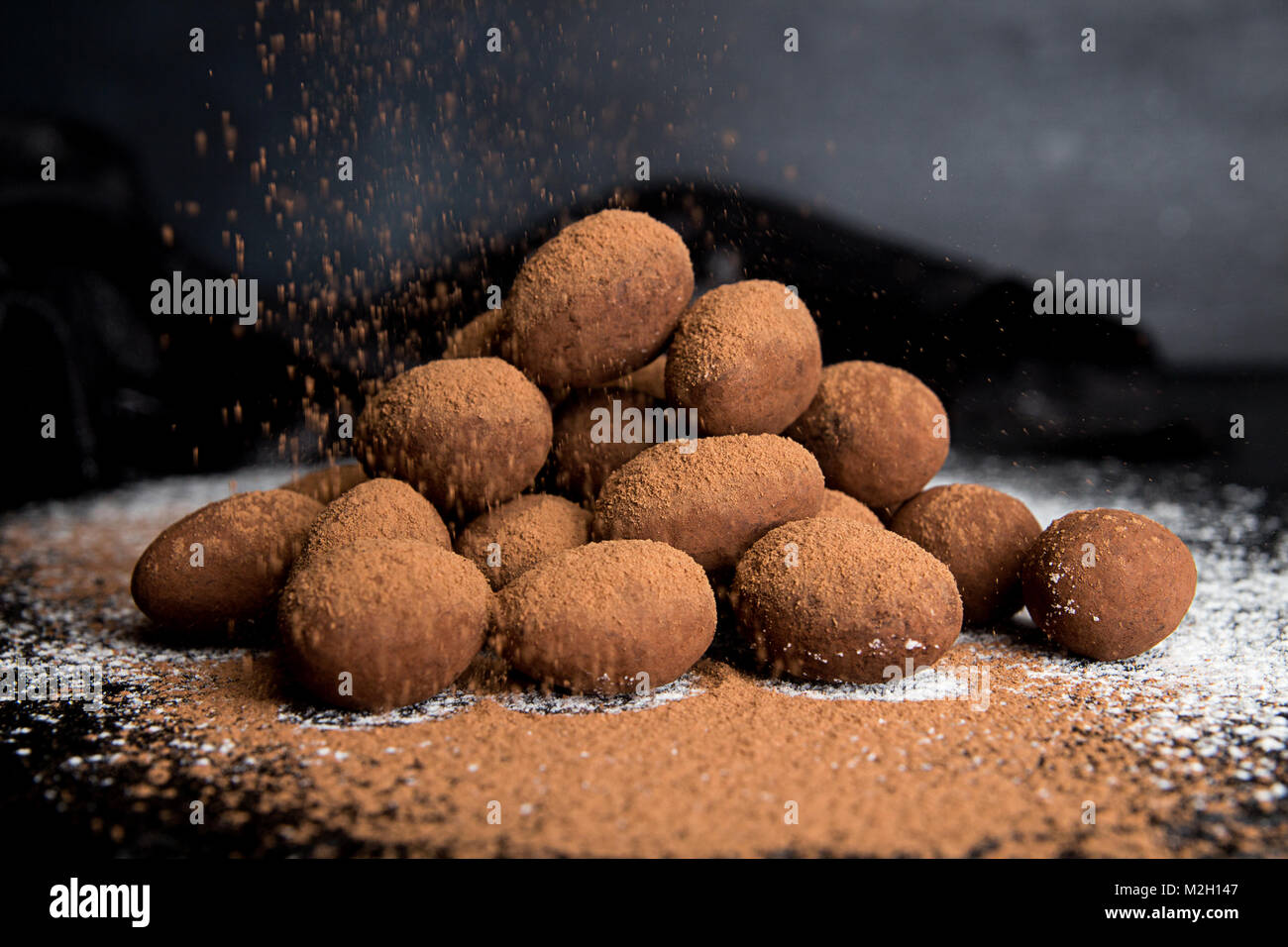 Bonbons Mandeln, umhüllt mit Schokolade Kakao einfügen auf dunklen schwarzen Hintergrund. Kakaopulver strewing auf Süßigkeiten. Stockfoto