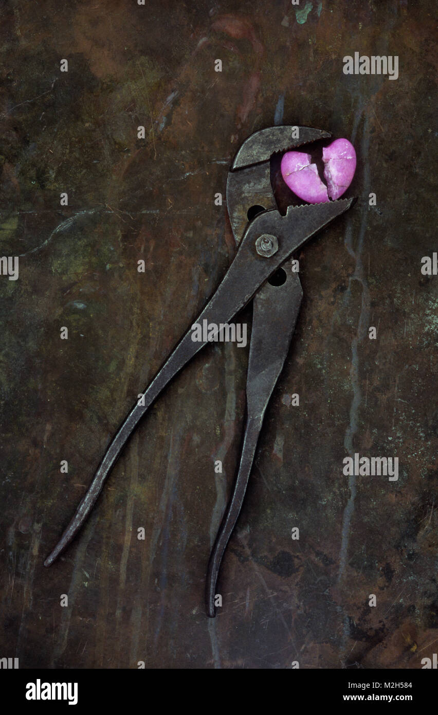 Viel verwendet, einstellbaren Schraubenschlüssel liegen auf angeschlagene Metall- und greifen ein Split rosa Stein Herz Stockfoto