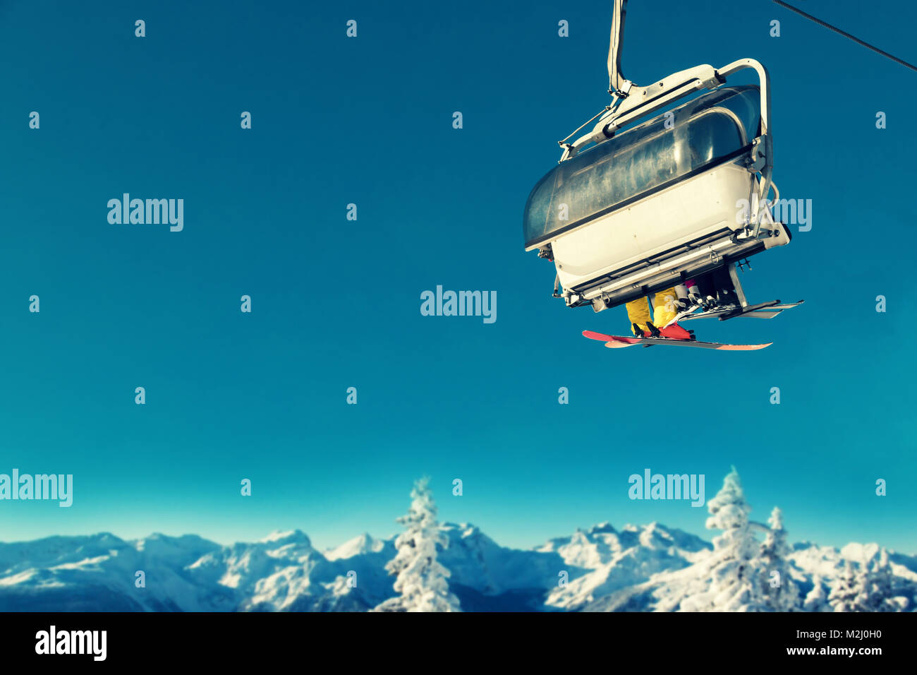 Menschen in Sesselbahn am Skigebiet über schneebedeckte Bäume und Berge Stockfoto