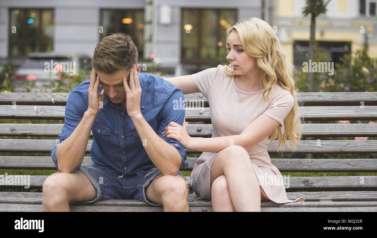 Besorgt Kerl sitzt auf der Bank, Freundin beruhigt ihn, Probleme, Support, Video Stockfoto
