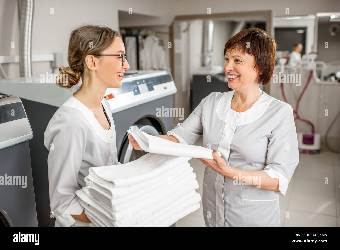 Senior washwoman mit jungen Assistenten in der Wäscherei Stockfoto