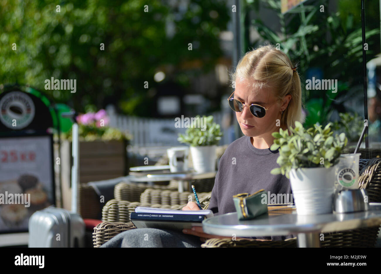 Eine blonde Studentin ein Buch lesen und dabei einen Kaffee am Morgen. Oslo, Norwegen Stockfoto