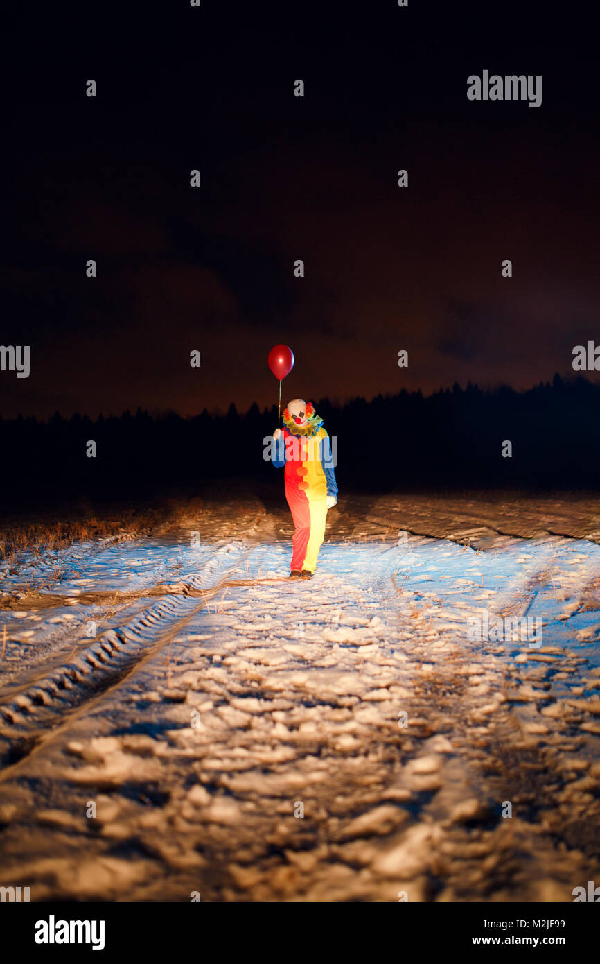 Foto aus der Ferne im vollen Wachstum der Clown mit bunten Luftballons bei Nacht Stockfoto