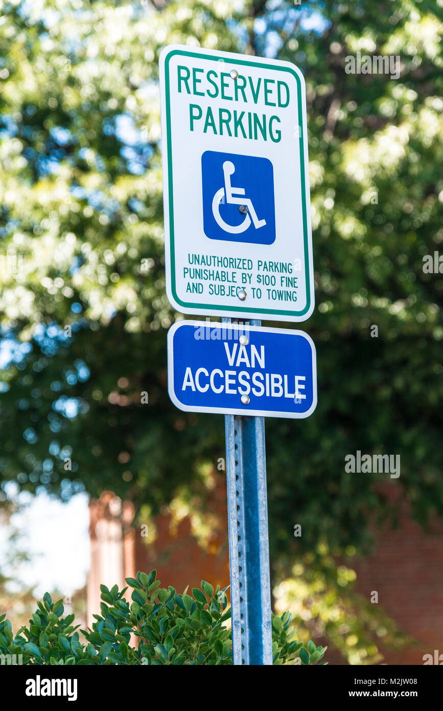 Vertikale Aufnahme eines behinderten Parkplatz Schild mit 15 Meilen pro Stunde Zeichen unten. Aus Bäumen und einem Gebäude im Hintergrund. Stockfoto