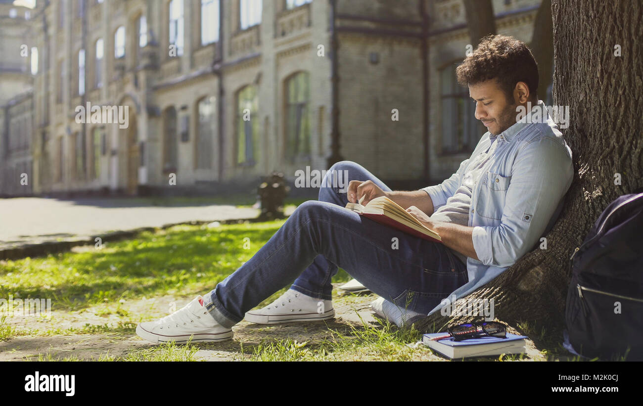 Mixed-race Kerl sitzen unter Baum im Park, reading book, Freizeit, Hobby Stockfoto