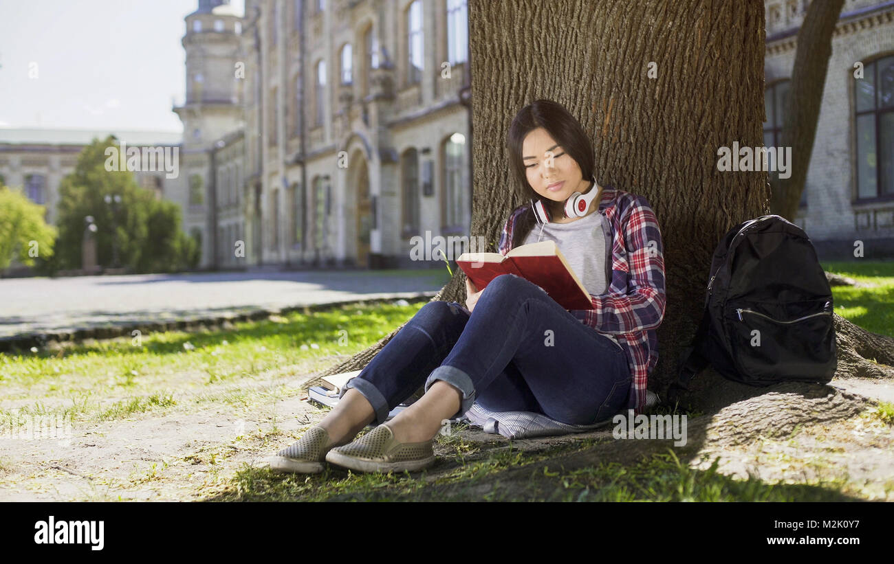 Gemischt weiblich sitzen unter Bäumen, lesen Lieblingsbuch, packende Handlung, verfasst Stockfoto