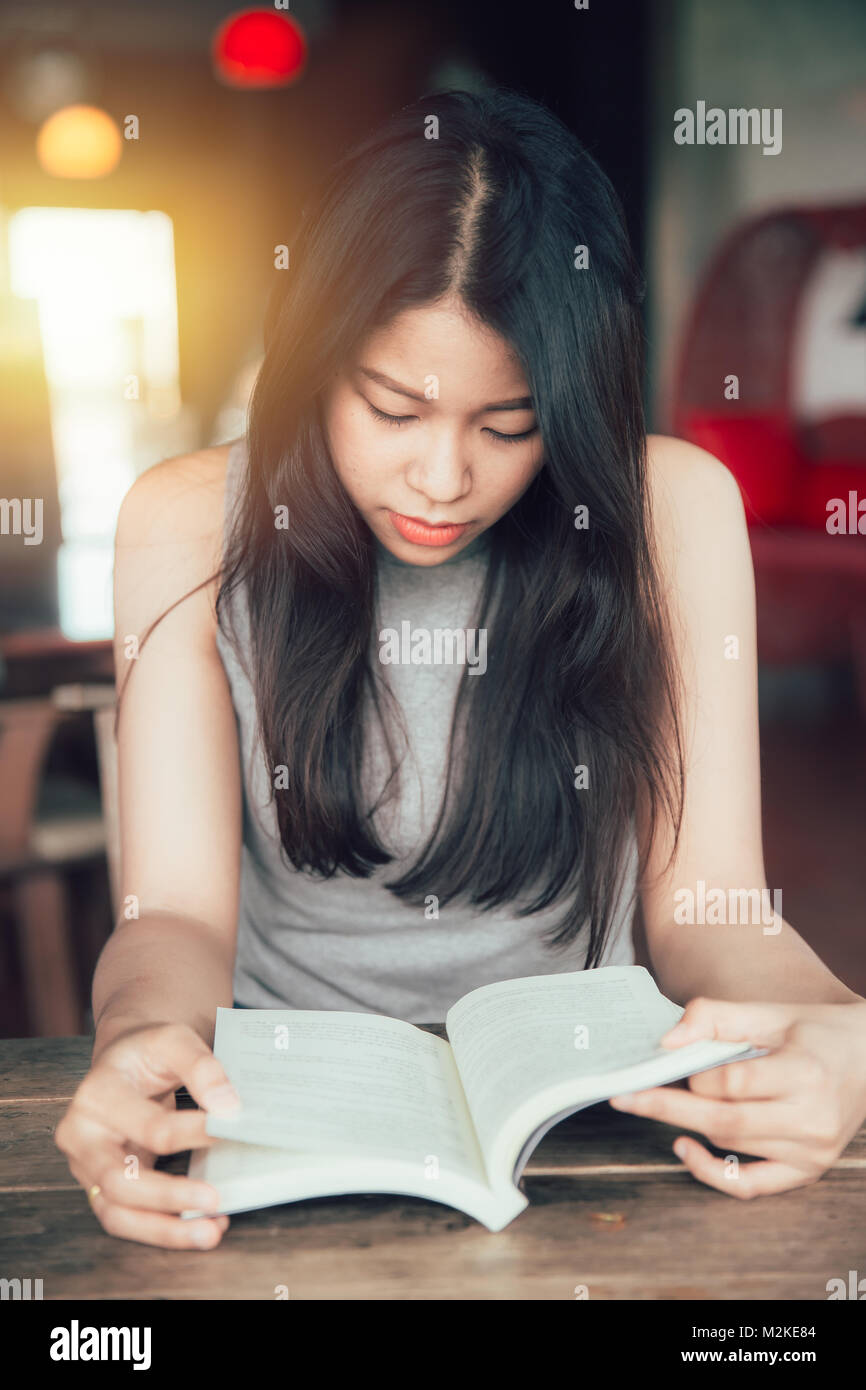 Casual Asian Girl focus suchen ein Buch lesen im Cafe vertikaler Stockfoto