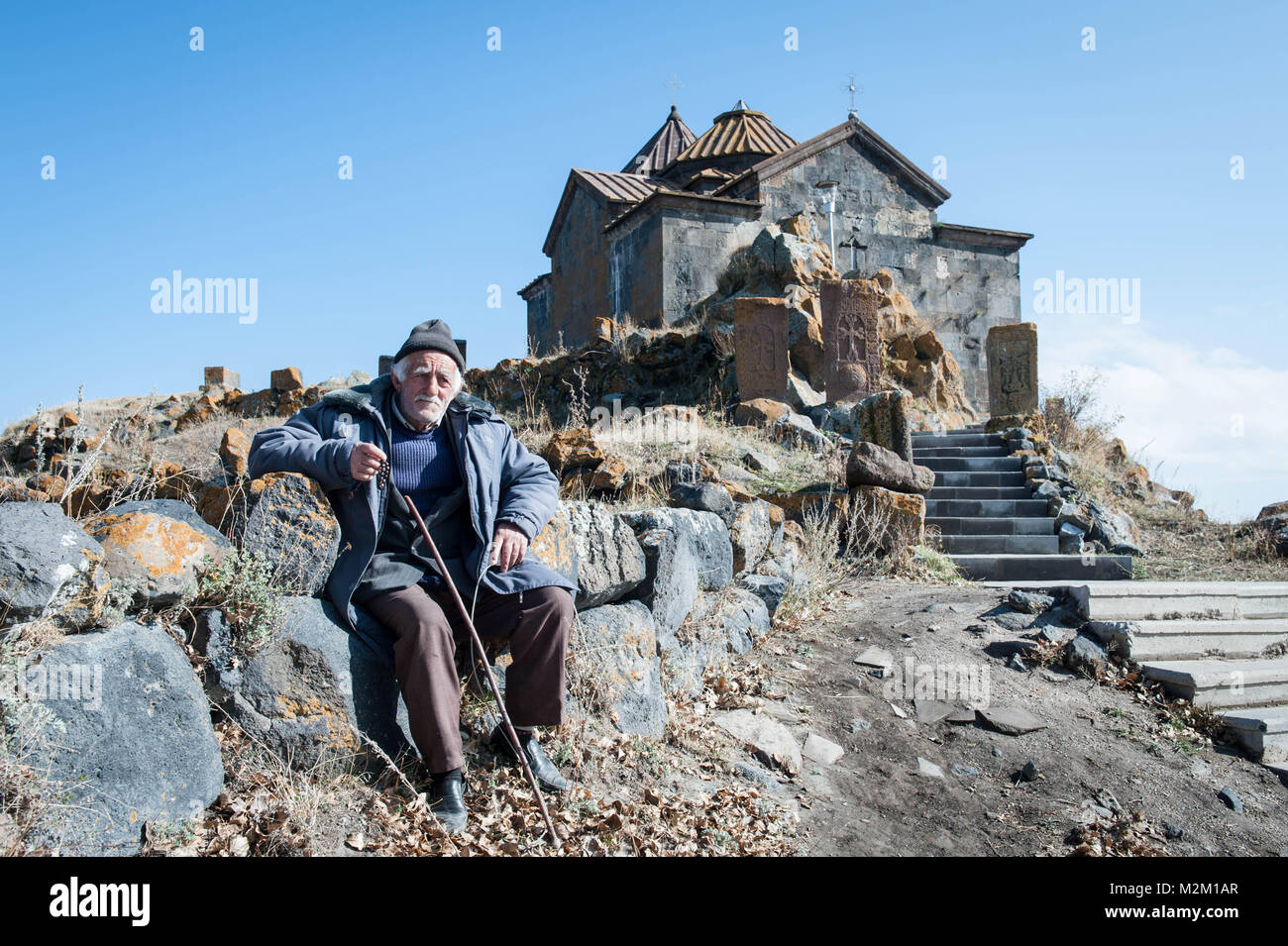 Alte Mann sitzt in der Nähe des Komplex von Sevanavank besteht aus Sts. Kirchen Arakelots und Karapet. Stockfoto