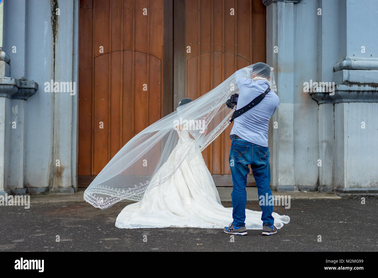 Leger gekleidet Hochzeit Fotograf nimmt Fotos einer Braut in ein eindrucksvolles weißes Kleid an den Türen von ihr ausgewählten Kirche. Stockfoto