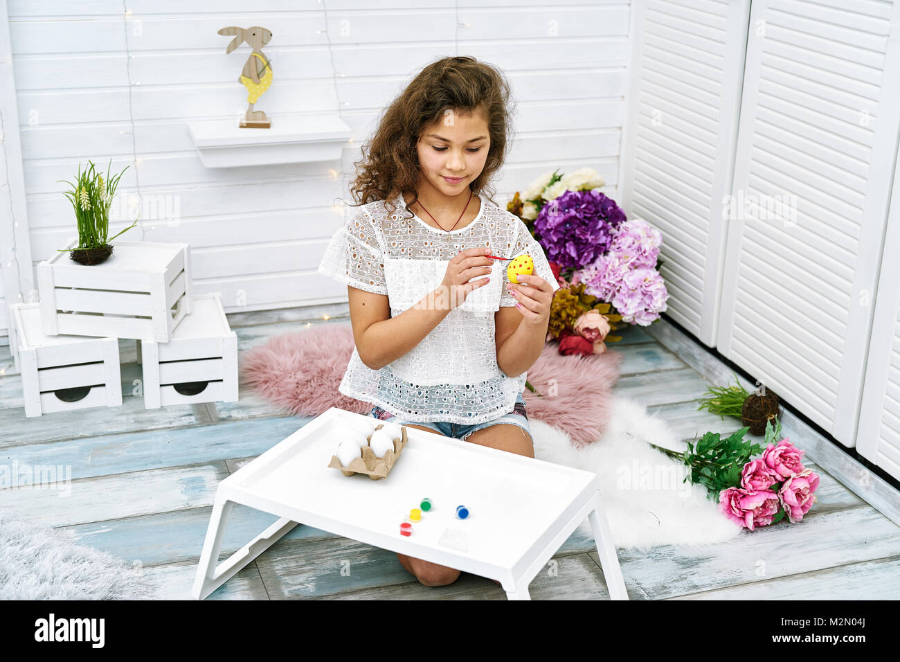 Zehn Jahre Mädchen malen Eier für das Osterfest in hellen, weißen Zimmer Stockfoto