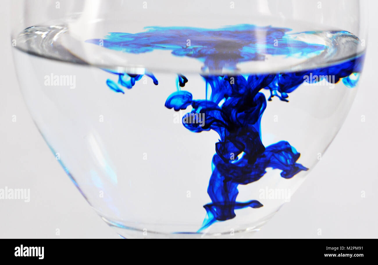 Wein Glas mit Wasser und blauen Tropfen Farbstoff gefüllt Stockfoto