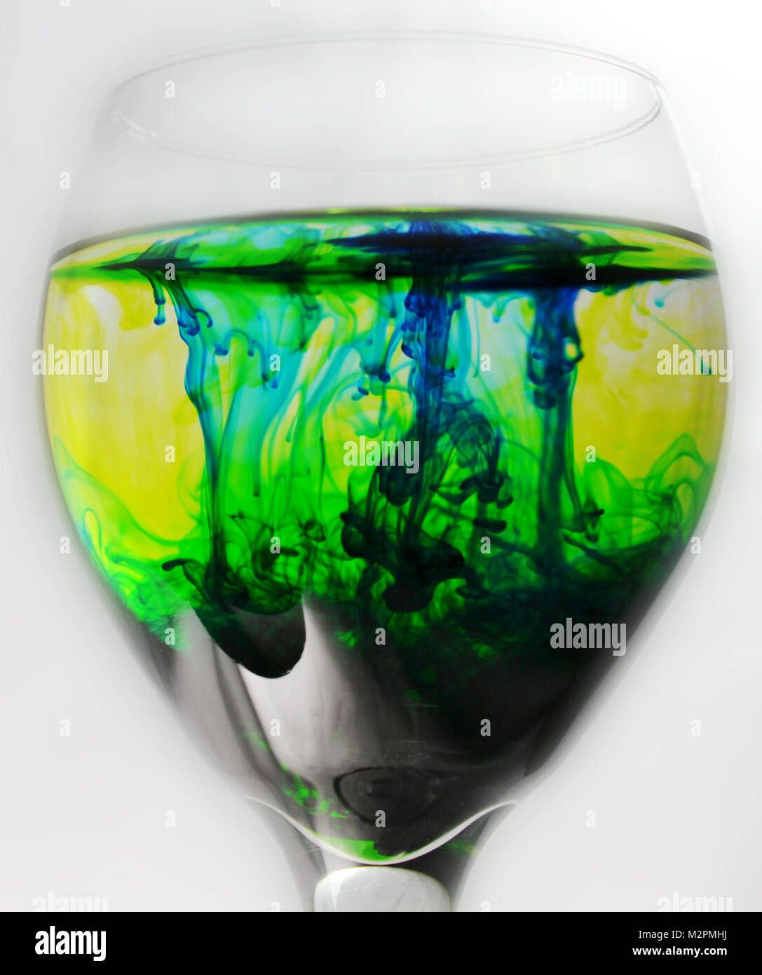 Wein Glas mit Wasser und grünen und blauen Tropfen Farbstoff gefüllt Stockfoto