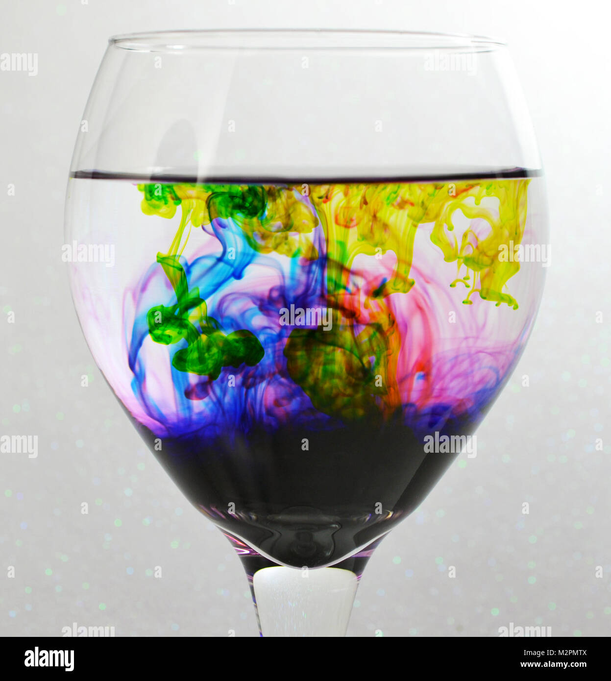 Wein Glas mit Wasser gefüllt und Grün, Blau, Rot und Lila Tropfen Farbstoff Stockfoto