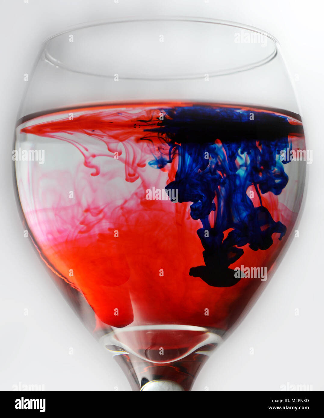 Wein Glas mit Wasser und roten und blauen Tropfen Farbstoff gefüllt Stockfoto