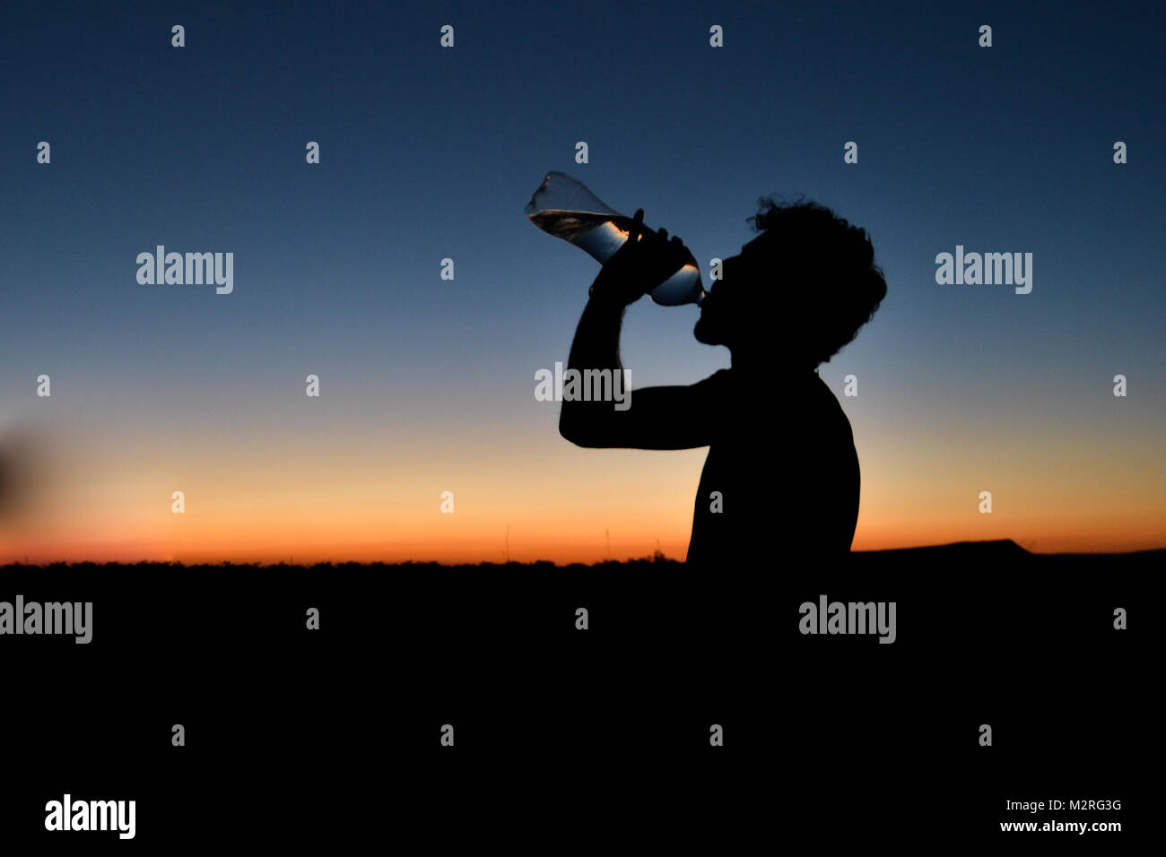 Junger Mann trinken Mineralwasser bei Sonnenuntergang in der Wüste Stockfoto