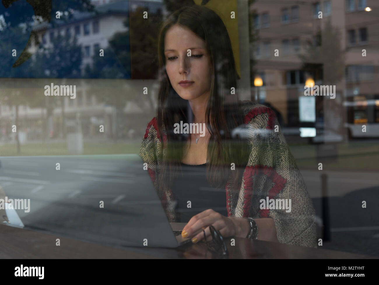 Junge Frau hinter dem Fenster auf dem Laptop, im Café, in der halb-portrait Stockfoto