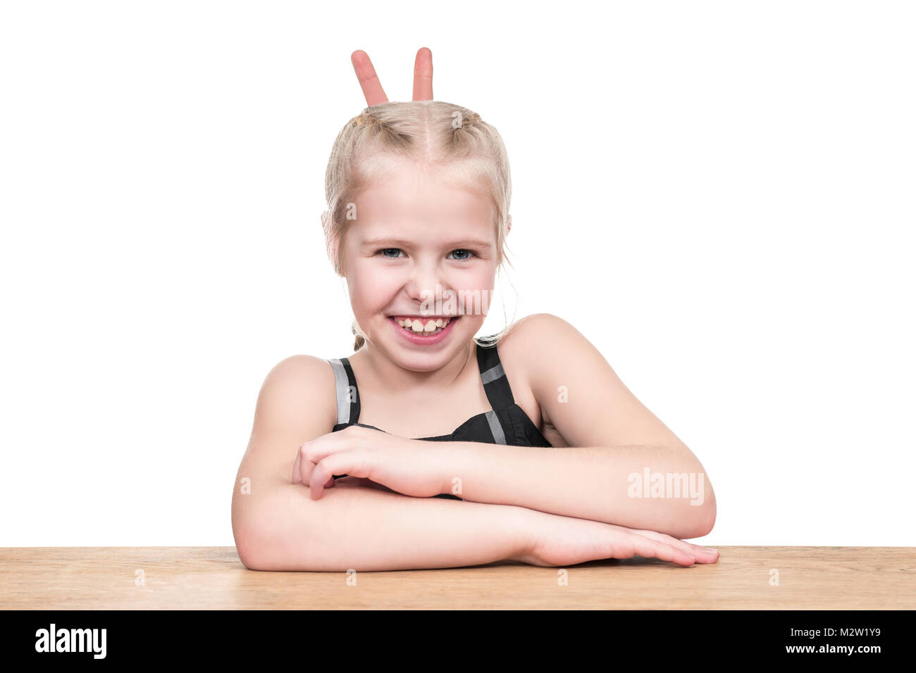 Porträt eines kleinen Mädchens an einem Holztisch sitzen mit Hörner von Fingern auf weißem Hintergrund Stockfoto