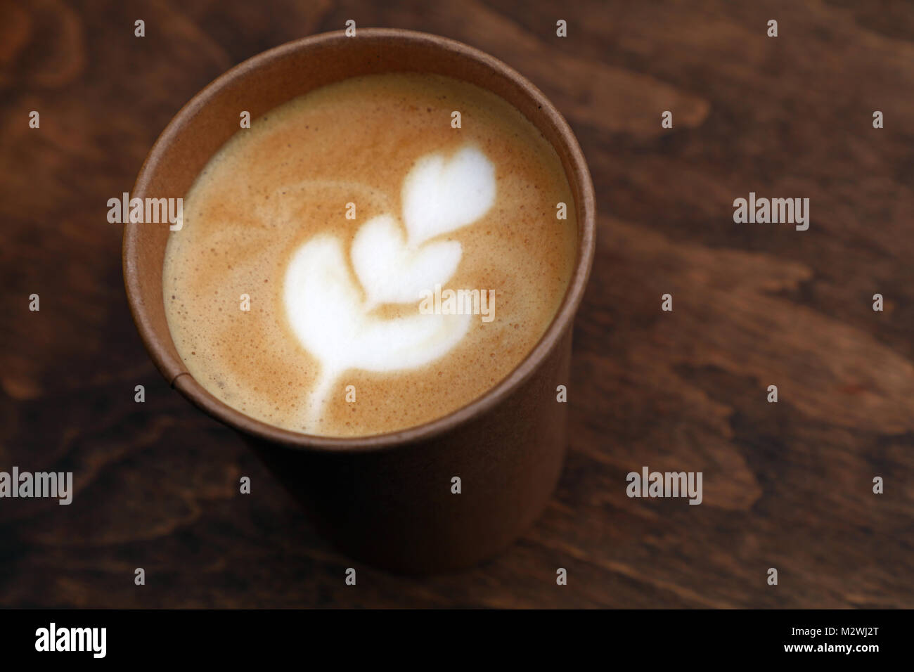 Nahaufnahme einer Latte Cappuccino Kaffee, Wegnehmen, in braunes Papier cup über Hintergrund der hölzernen Tisch, erhöhte Hohe Betrachtungswinkel Stockfoto