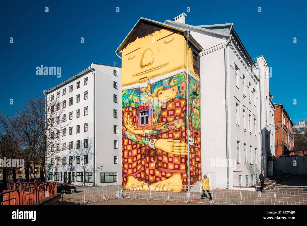 Minsk, Weißrussland. Graffiti oder Wandmalereien von Os Gemeos brasilianischen Street Art Künstler an der Wall von Brasilien Botschaft. Große gelbe Riese Sitzend mit seiner langen Beine Fol Stockfoto