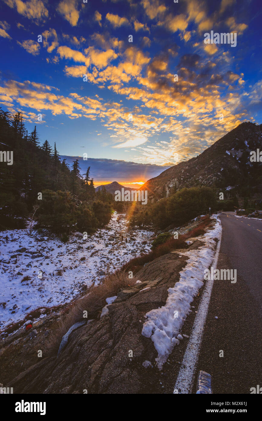 Sonnenuntergang an der schneebedeckten Mount Baldy im Winter mit einer Straße windet sich durch die hohen Gipfel und bunte Wolken im Himmel, San Gabriel Mountains Stockfoto