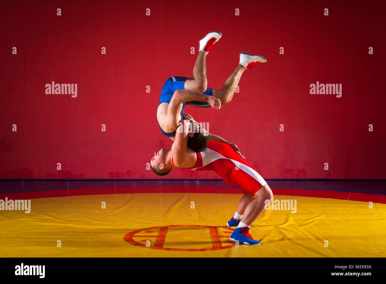 Zwei junge Männer in blauen und roten Ringen Strumpfhosen sind wrestlng und einen suplex wrestling auf einem gelben wrestling Teppich in der Turnhalle Stockfoto