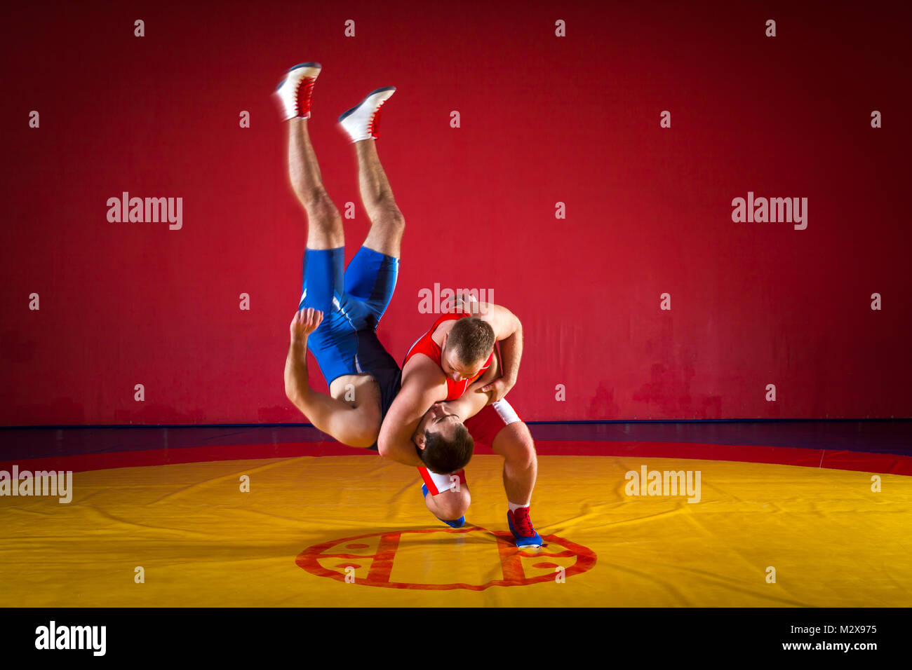 Zwei junge Männer in blauen und roten Ringen Strumpfhosen sind wrestlng und einen suplex wrestling auf einem gelben wrestling Teppich in der Turnhalle Stockfoto