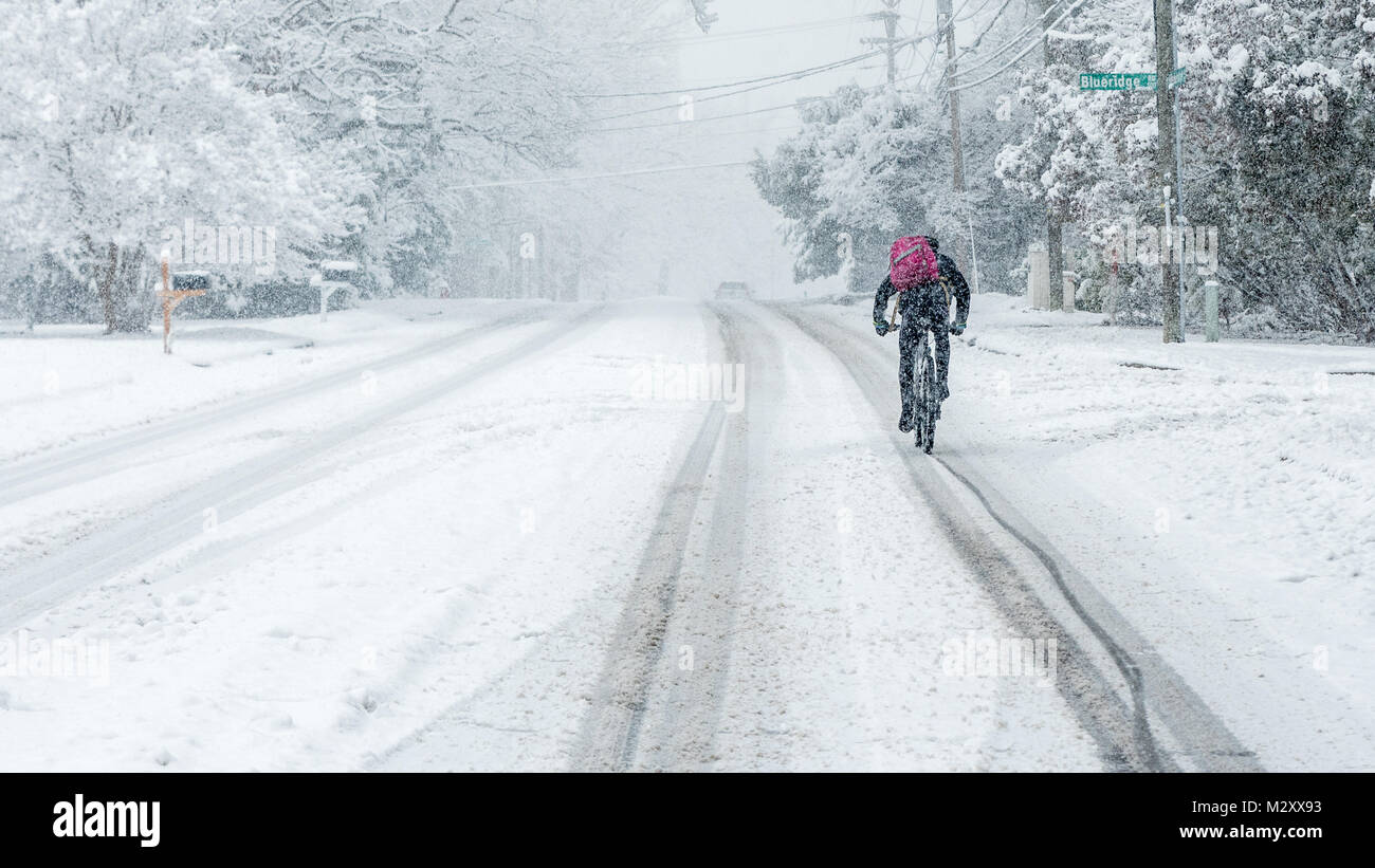 Mann, ein Fahrrad im Schnee auf einer Intown Straße mit lila Rucksack Stockfoto