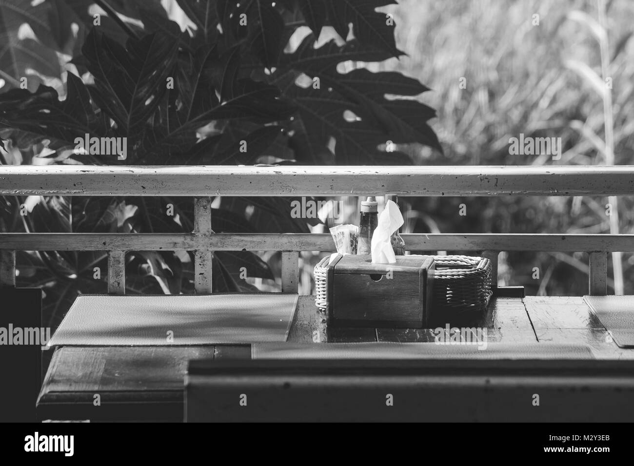 Holz- gewebe, und Garnieren in Warenkorb (Salz, Pfeffer, Zahnstocher, Soße) auf Tisch mit grünen Bäumen und Sonnenlicht Hintergrund in den Morgen. Stockfoto