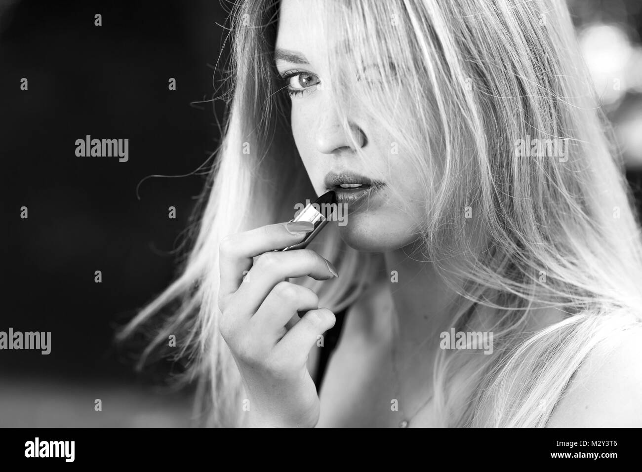 Schöne junge blonde Frau korrigiert - Anwendung der roten Lippenstift Make-up im Park. Konzept jugendlicher Lebensstil. Stockfoto