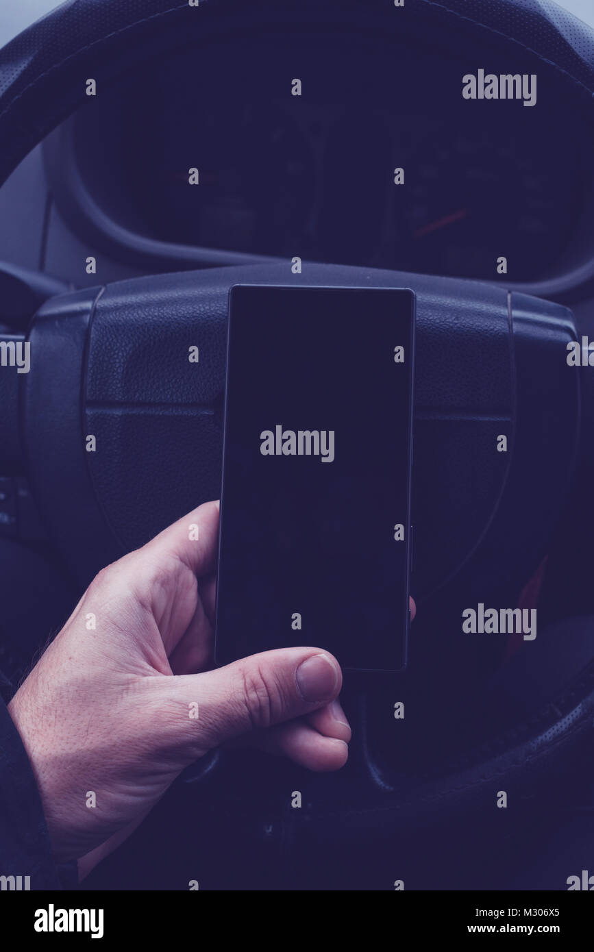 Mann mit Handy im Auto. Männliche hand mit modernen Smartphone über Lenkrad, Ultra Violet Schatten getönt Stockfoto