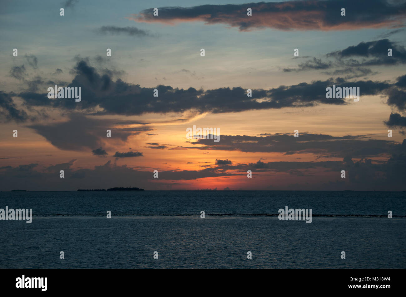 Orange Sonnenuntergang am Indischen Ozean: pink und orange blinkt, von der untergehenden Sonne, lange graue Kumuluswolken auf den sanften blauen Himmel. Stockfoto