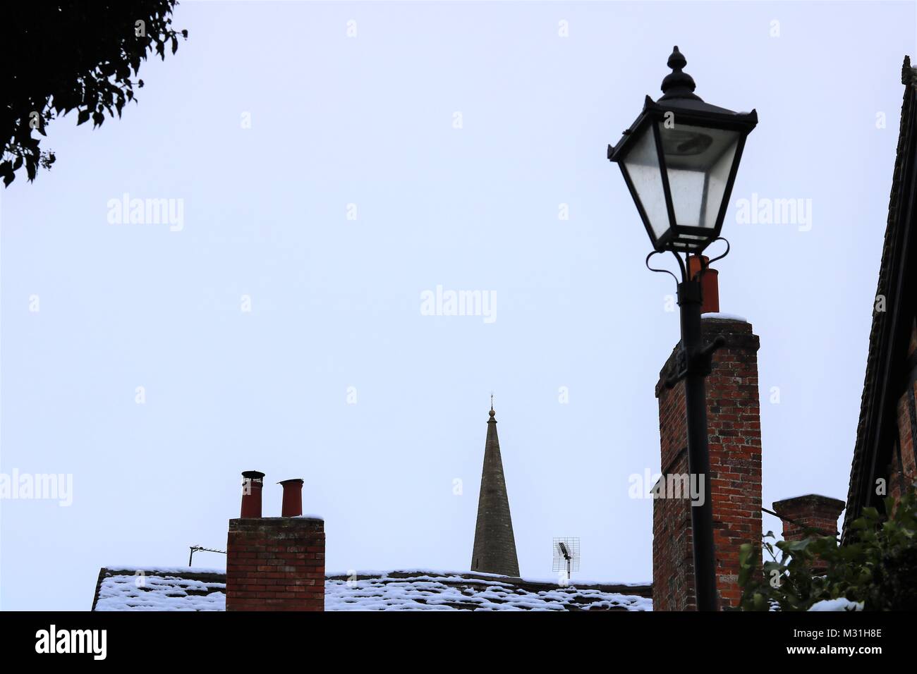 Buckingham, Großbritannien, Skyline Bild der alten Straßenlaterne, chimney pot und Kirchturm mit einem Abstauben des Schnees gegen einen schwachen blauen Himmel im Winter Stockfoto