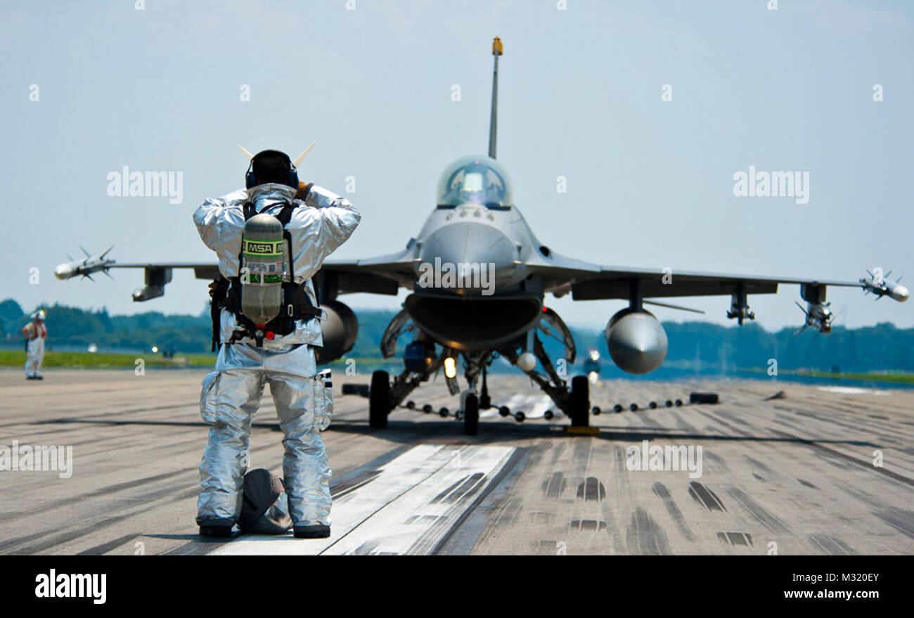YOKOTA AIR BASE, Japan - ein Feuerwehrmann aus 374 Bauingenieur Squadron gibt Richtung zu einer F-16 Falcon pilot Yokota Air Base, Japan, 10. Juli 2013. Verschiedene Abteilungen von 374 CES, einschließlich Feuerwehr, während der Festnahme gang Prüfung teilgenommen. Die zwei F-16 von Misawa Air Base, Japan, mit der Prüfung des Systems unterstützt. (U.S. Air Force Foto von Airman 1st Class Soo C. Kim) F-16 Fighting Falcon Pilot von # FIRMA PACOM Stockfoto