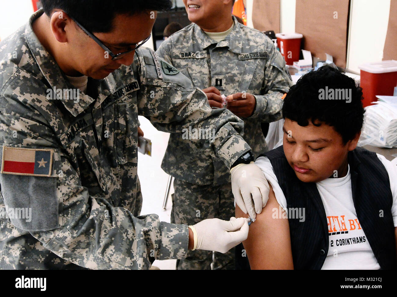 Texas State Guard Kapitän Rexie Pajarillaga von Houston Medical Brigade verwaltet einen von vier Impfungen, die Juan Carlos Martinez, 13, at Palmview High School in Palmview, Texas empfangen, während des Betriebs Lone Star Montag, 29. Juli 2013. Betrieb Lone Star ist ein wochenlanges, low-no-cost Medical screening Service und Emergency Readiness Übung, ist die größte öffentliche Gesundheit humanitären Bemühungen, dieser Art, im Land. Die Übung lief gleichzeitig an fünf Standorten entlang der South Texas Grenzgebiet von Brownsville, Texas, nach Laredo, Texas, 29. Juli Aug 2, 2013. (U.S. Armee Nati Stockfoto