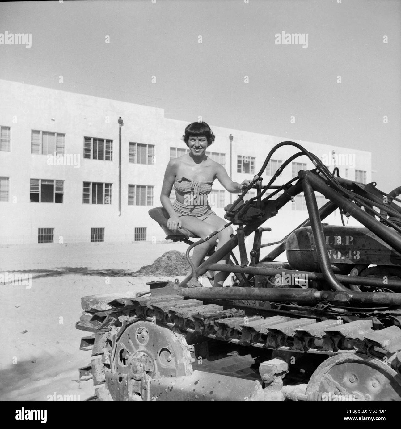 Eine junge Frau in einem Badeanzug sitzt auf einem Bulldozer, Ca. 1948. Stockfoto
