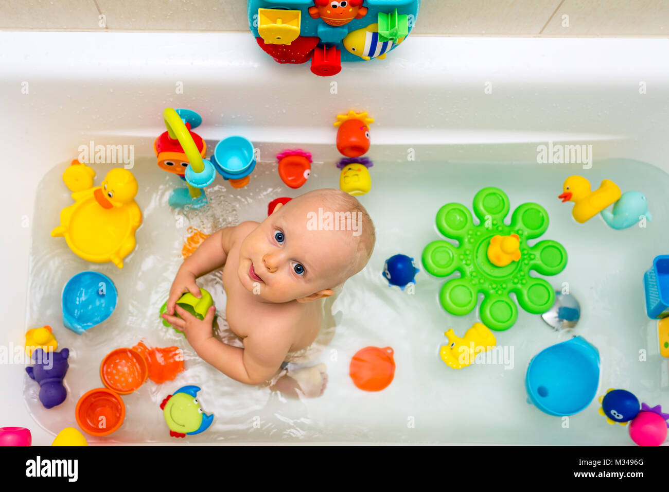 Baby in der Badewanne und spielt in einer Badewanne mit bunten Spielzeug. Lächelnd kleine Zicklein im Badezimmer an der Kamera schaut. Kleinkinder spielen, Spaß haben und washin Stockfoto