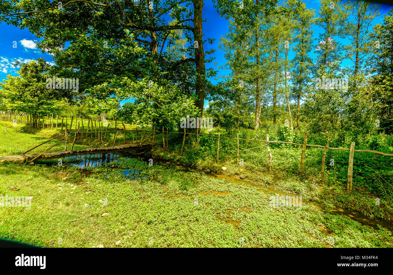 Eine ländliche Szene mit Brücke im Vordergrund, einem kleinen Fluss im Hintergrund läuft. Stockfoto